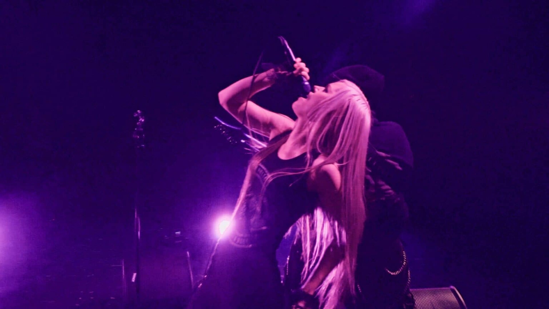 Purple stage light and a raised mic — still from the "Forsaken" music video